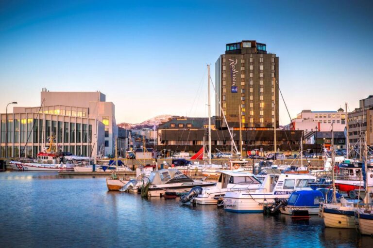 Harbor scene with moored boats and a tall hotel building in the background at sunset