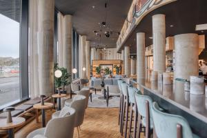 Bright modern cafe interior with a long bar counter, teal upholstered bar stools, and large windows along the left wall.