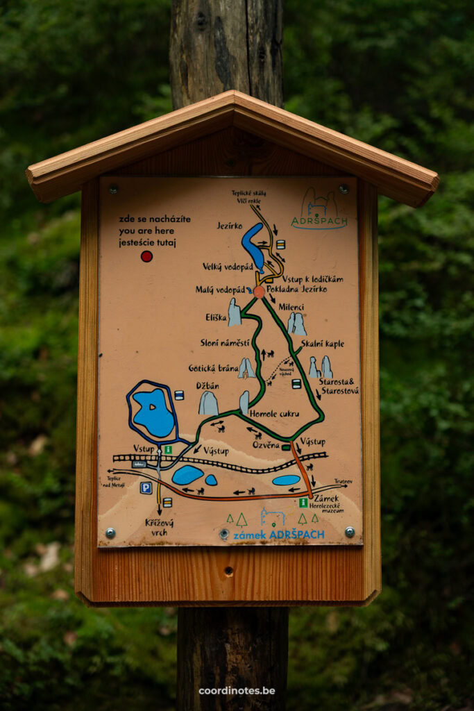 Wood-framed trail map sign in a forest, showing paths and landmarks around Adršpach Castle (Adršpach rocks).