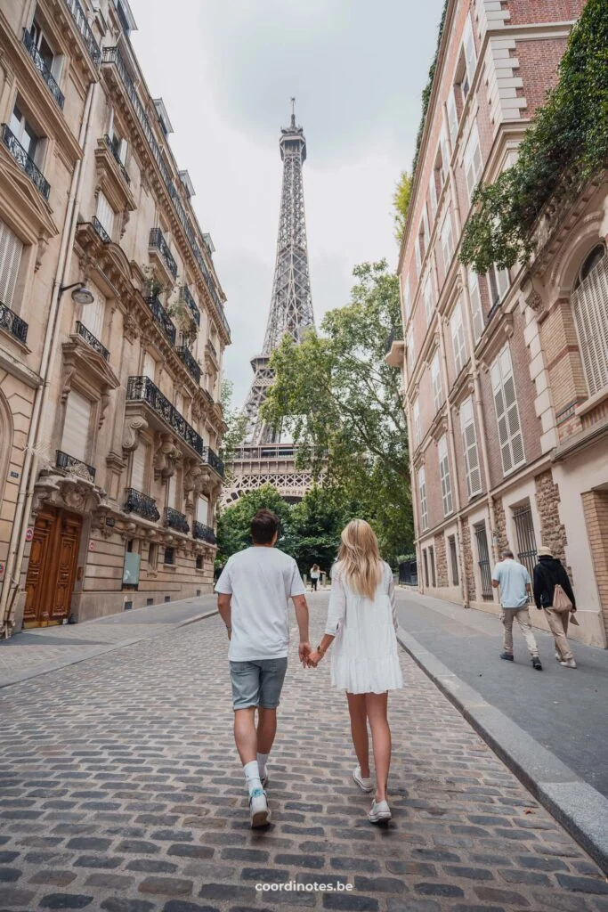 The two of us walking hand in hand through a cobble stone street towards the Eiffel tower in the background. On both sides of the street you see typical Parisian buildings.