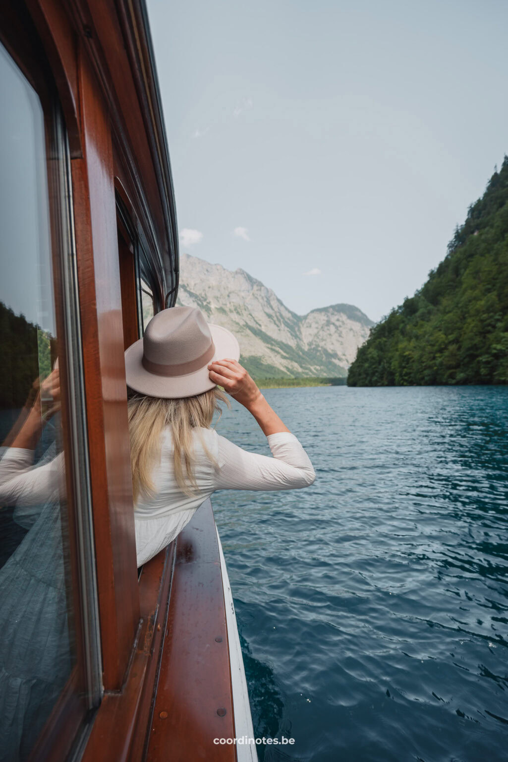 Sarah die uit de raam van een elektrische boot hangt terwijl ze kijkt naar de bergen in de achtergrond bij Königssee