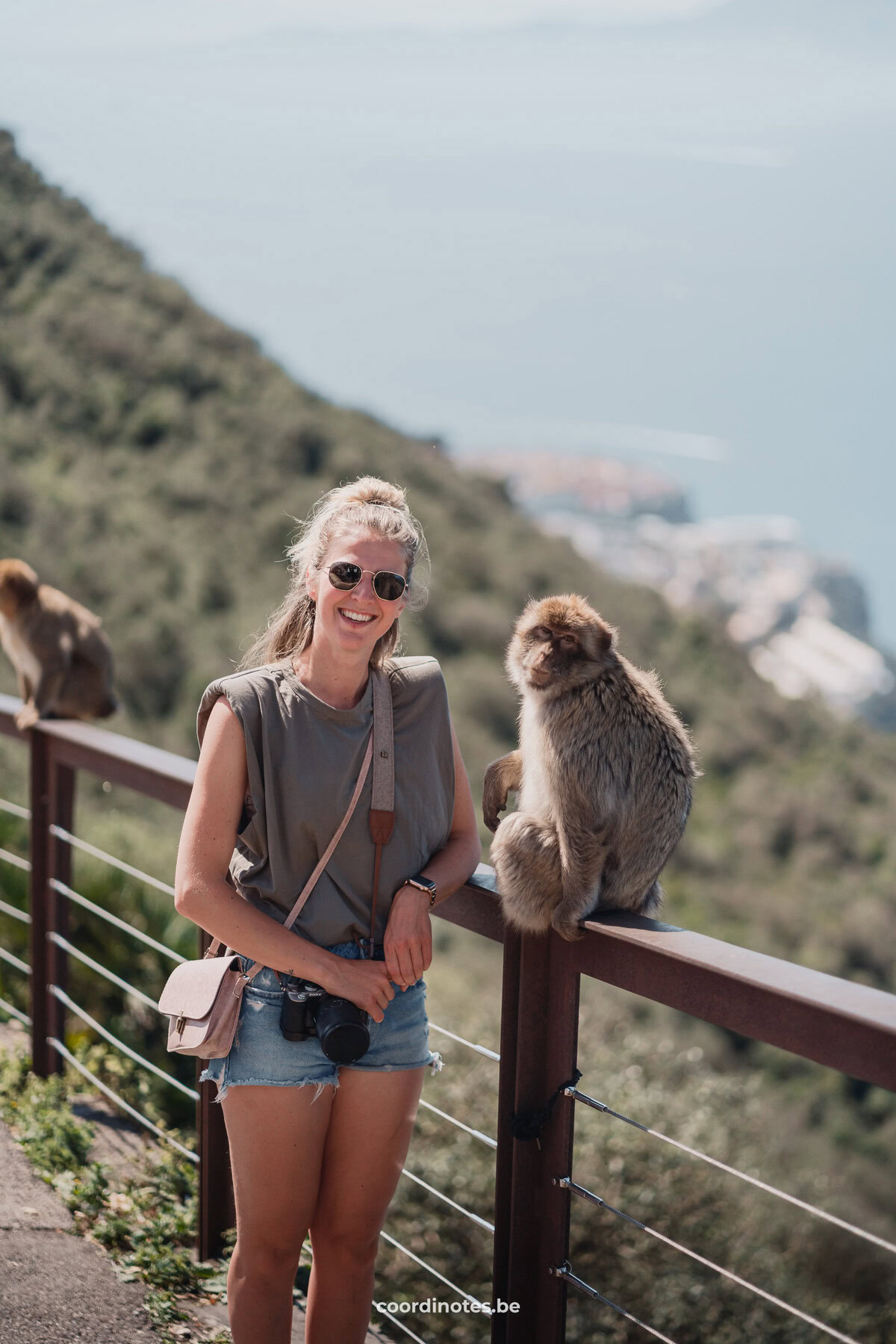 Sarah naast een berberaap op een hek in Gibraltar met de zee in de achtergrond.