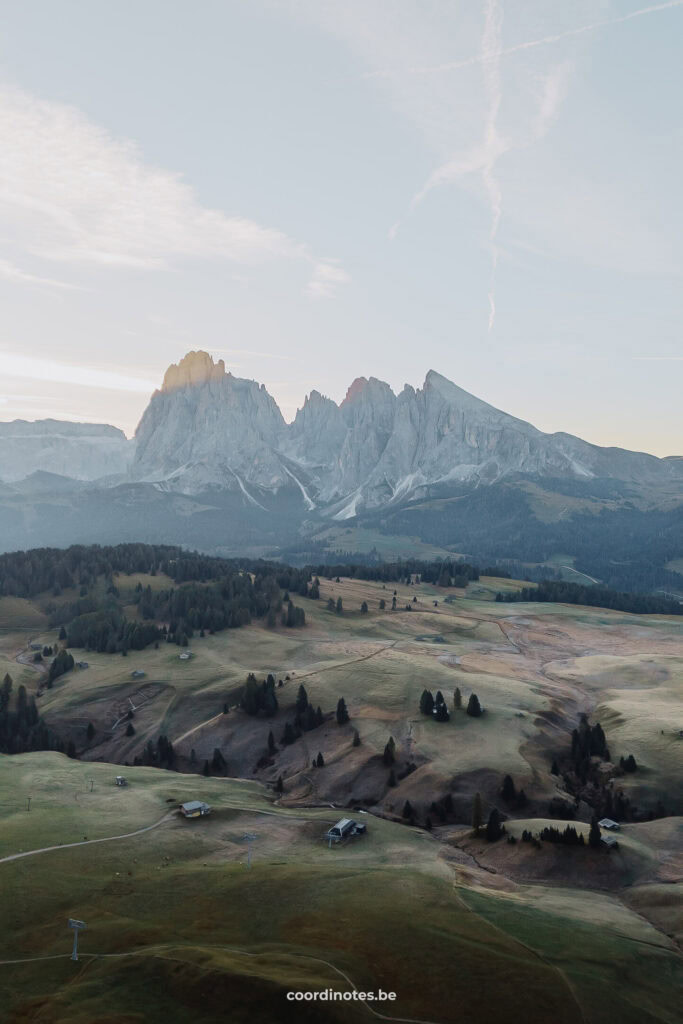 Het uitzicht over de bergweide van Seiser Alm gevuld met bomen, houten cabines en een grote bergketen op de achtergrond.