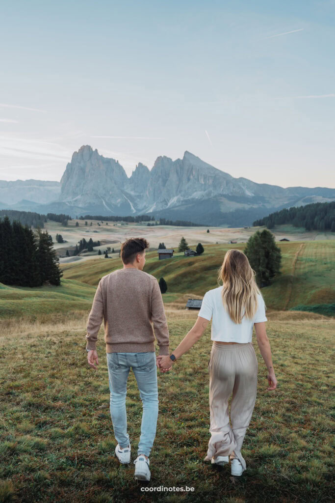 Wij twee die hand in hand wegwandelen op het gras met de grote bergweide van Seiser Alm en een grote bergketen op de achtergrond tijdens zonsopgang.