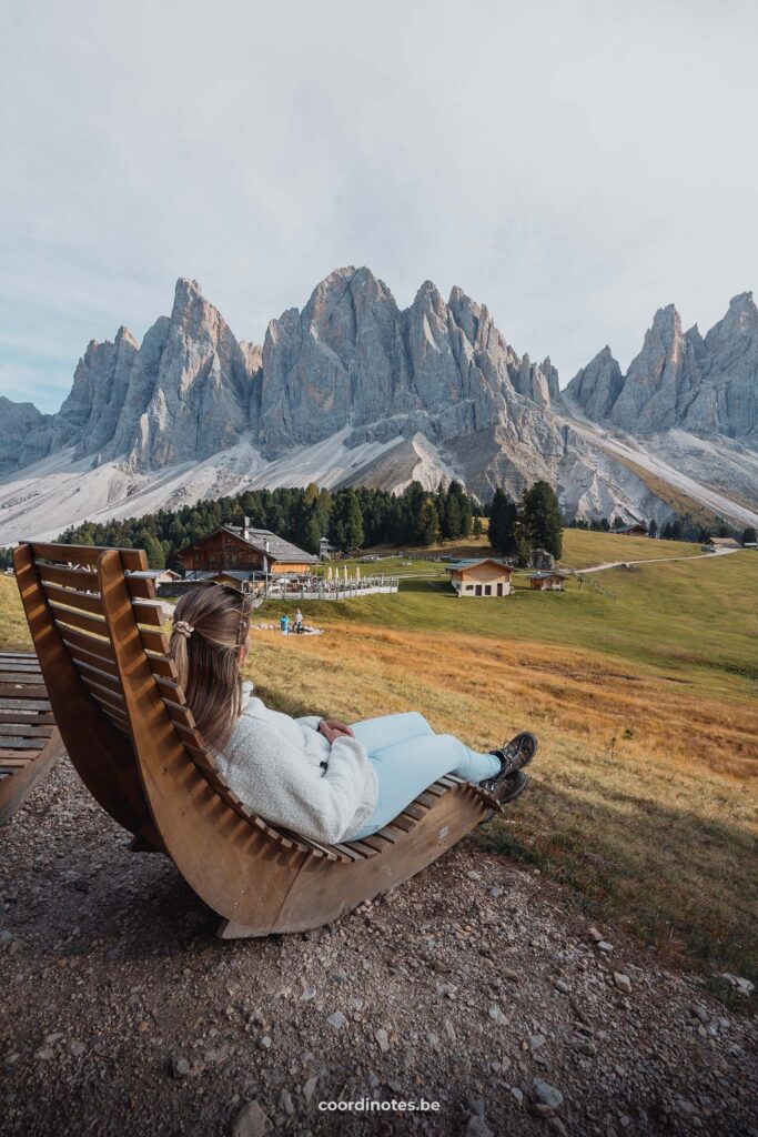 Sarah sitting on a long chair watching at the Geisler Alm and the mountain peaks in the background