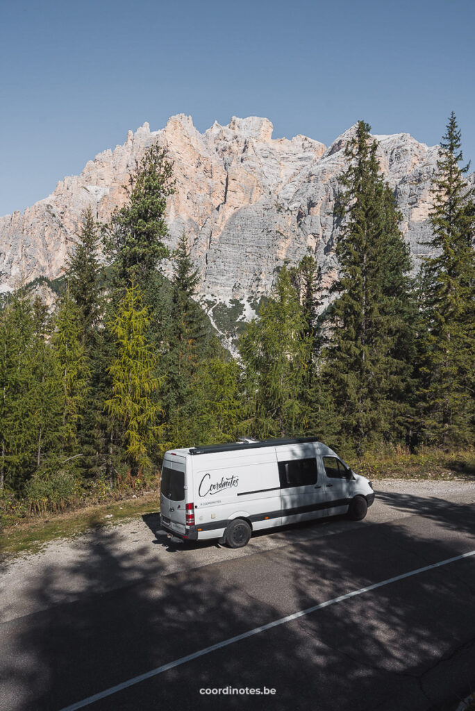 Our campervan next to the road in front of pine trees and the mountain peaks in the background.