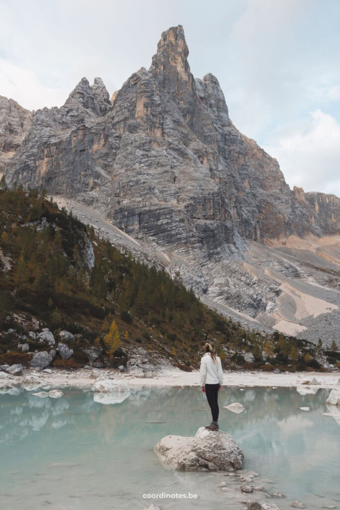 Sarah op een rots in het turquoise blauwe water van Lago di Sorapis met een dramatische bergtop op de achtergrond tijdens zonsopgang