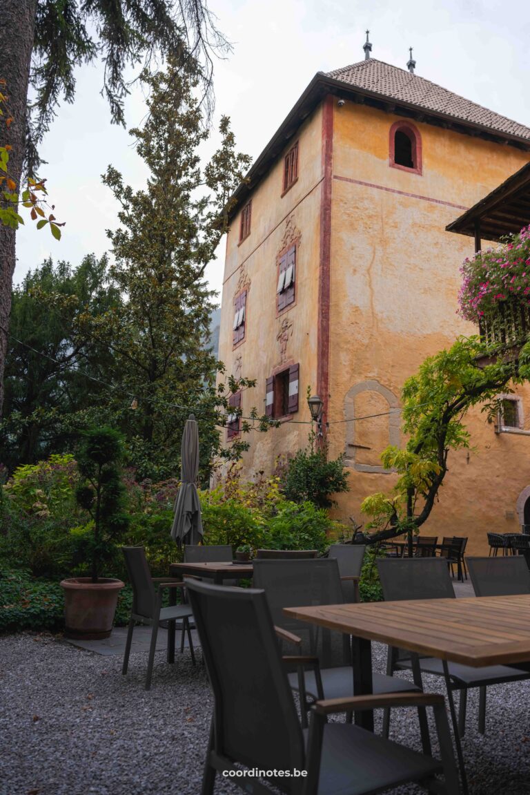 A terrace next to a yellow castle-like building surrounded by green plants.