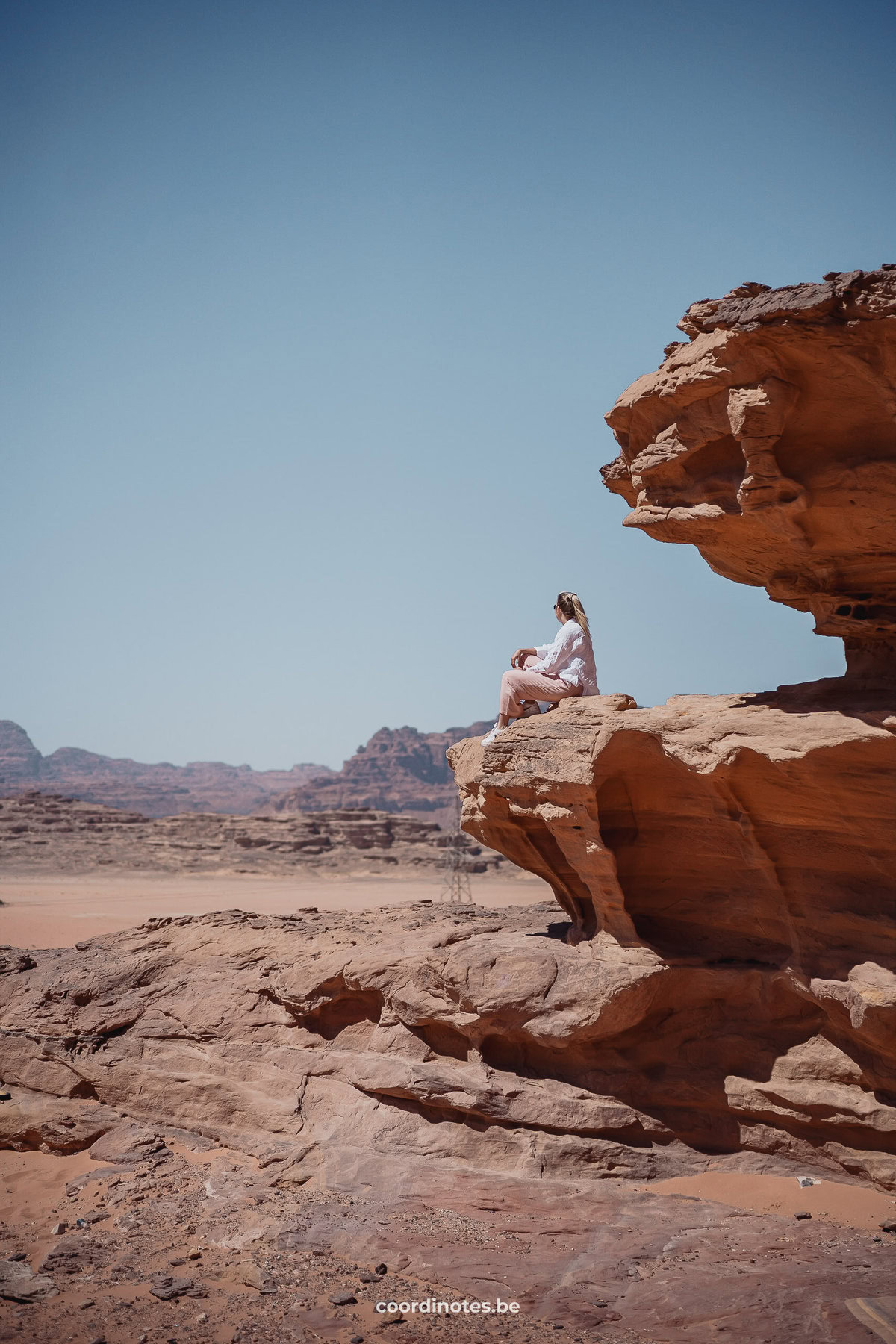 Sarah die op een grote rots zit terwijl ze kijkt naar het mooi uitzicht over de Wadi Rum woestijn in de achtergrond