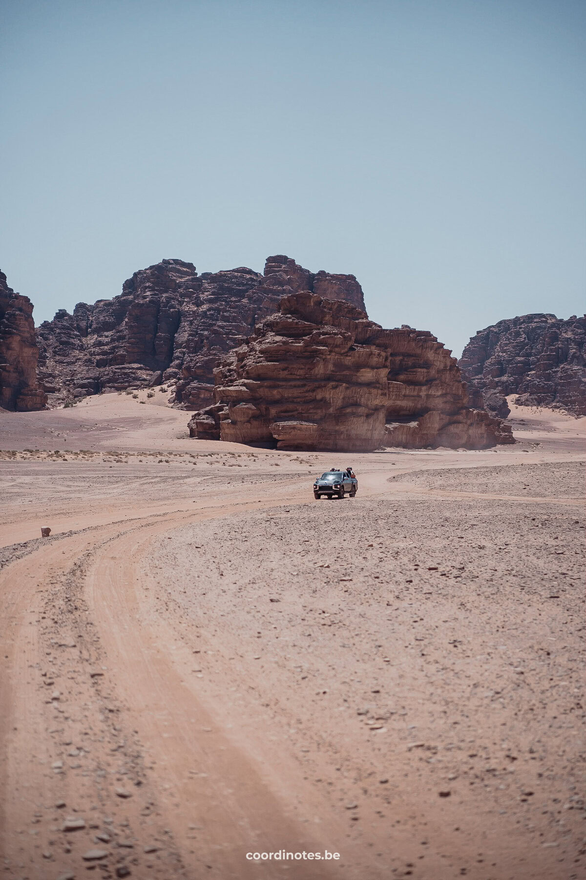 Een jeep die door de Wadi Rum woestijn rijdt tijdens een Wadi Rum Jeep safari met grote rotsen op de achtergrond