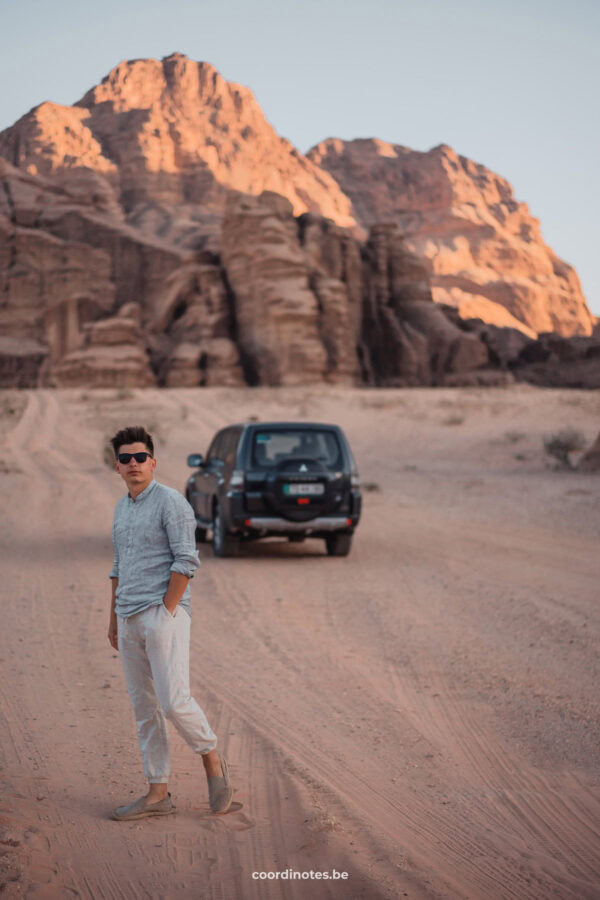 Cédric walking in the Wadi Rum desert with our jeep and huge rock formations in the background during sunset.