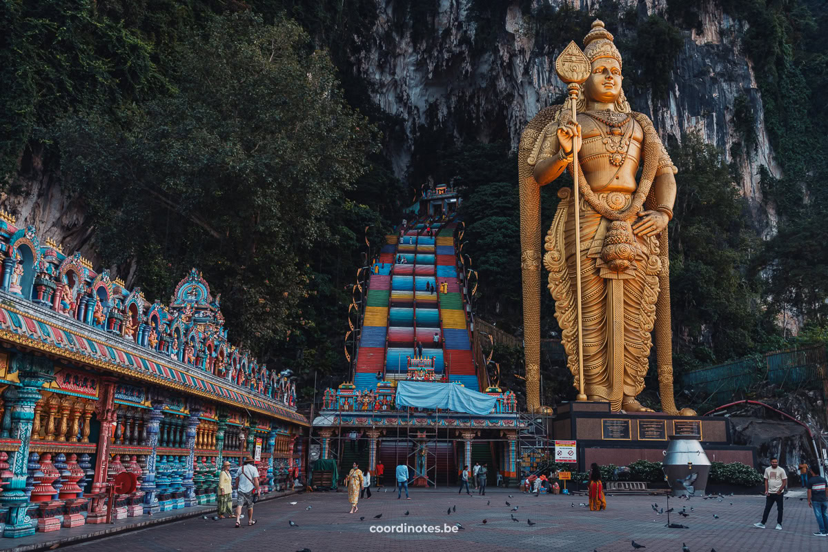 The rainbow stairs leading to the Batu Caves in the limestone mountains with one the left side a temple and on the right side the big golden statue of Lord Murugan, the Hindu god of war.