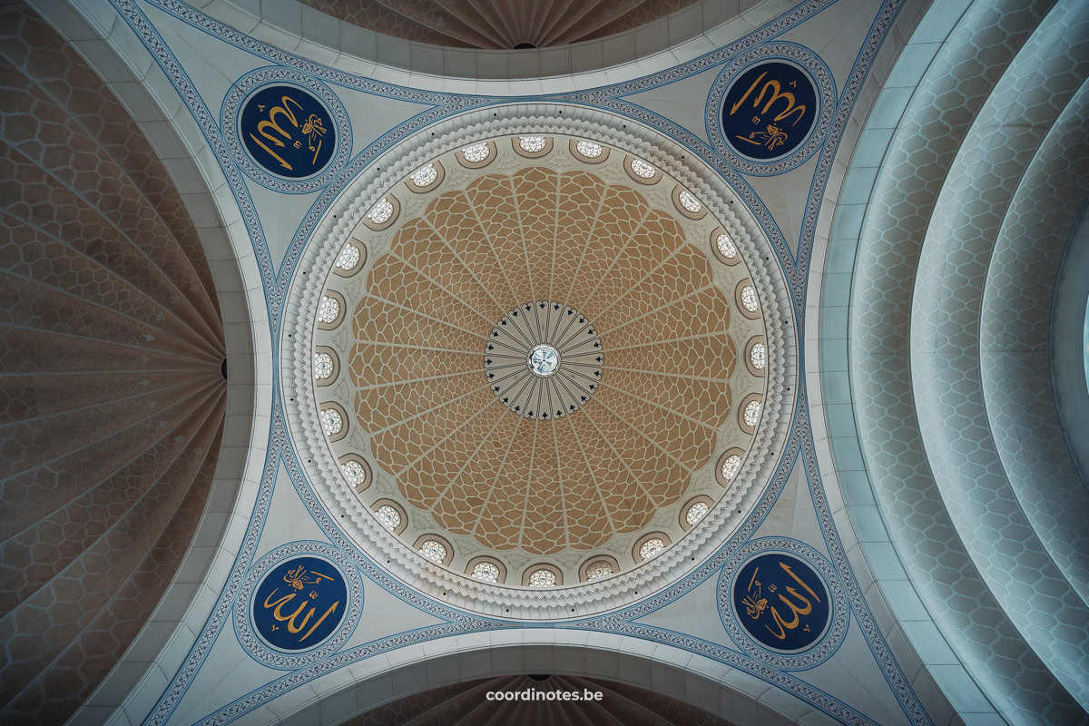 Bottom view on arches and a couple of the ceiling of the Federal Territory Mosque decorated with a yellow pattern.