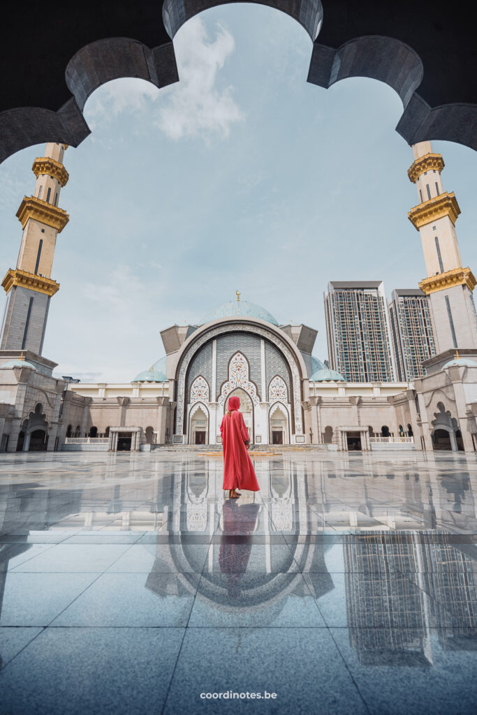 Sarah walking in a pink dress on the big square of the Federal Territory mosque with the beautifully decorated facade and two golden minarets on both sides.