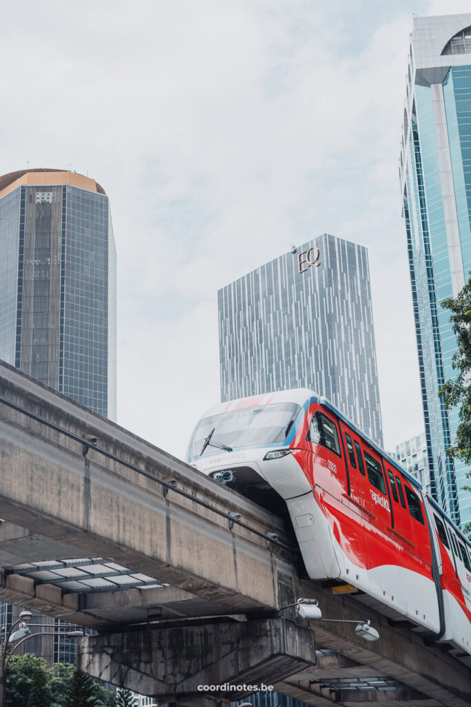 Bottomview of a sky metro riding over the sky rails with three skyscrapers in the background.