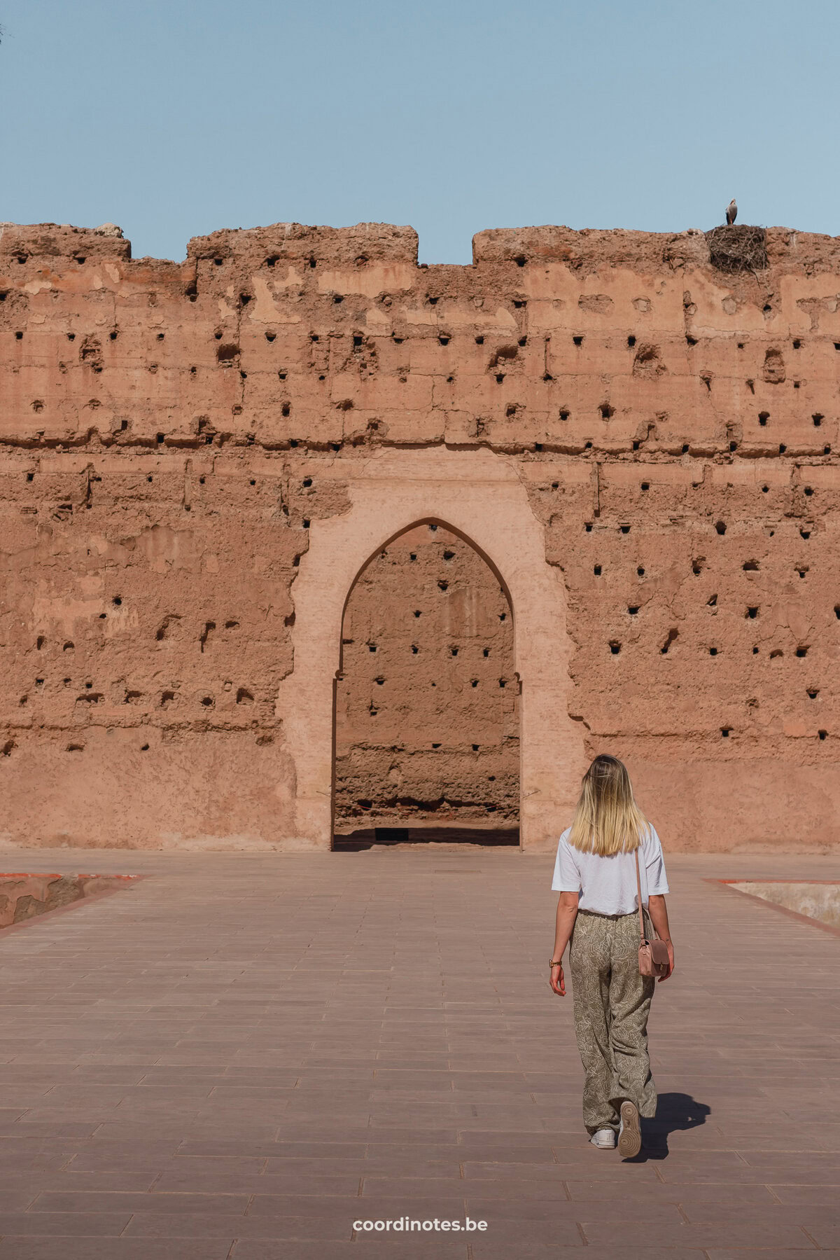 Sarah walking towards a big open gate in an orange wall in El Badi Palace