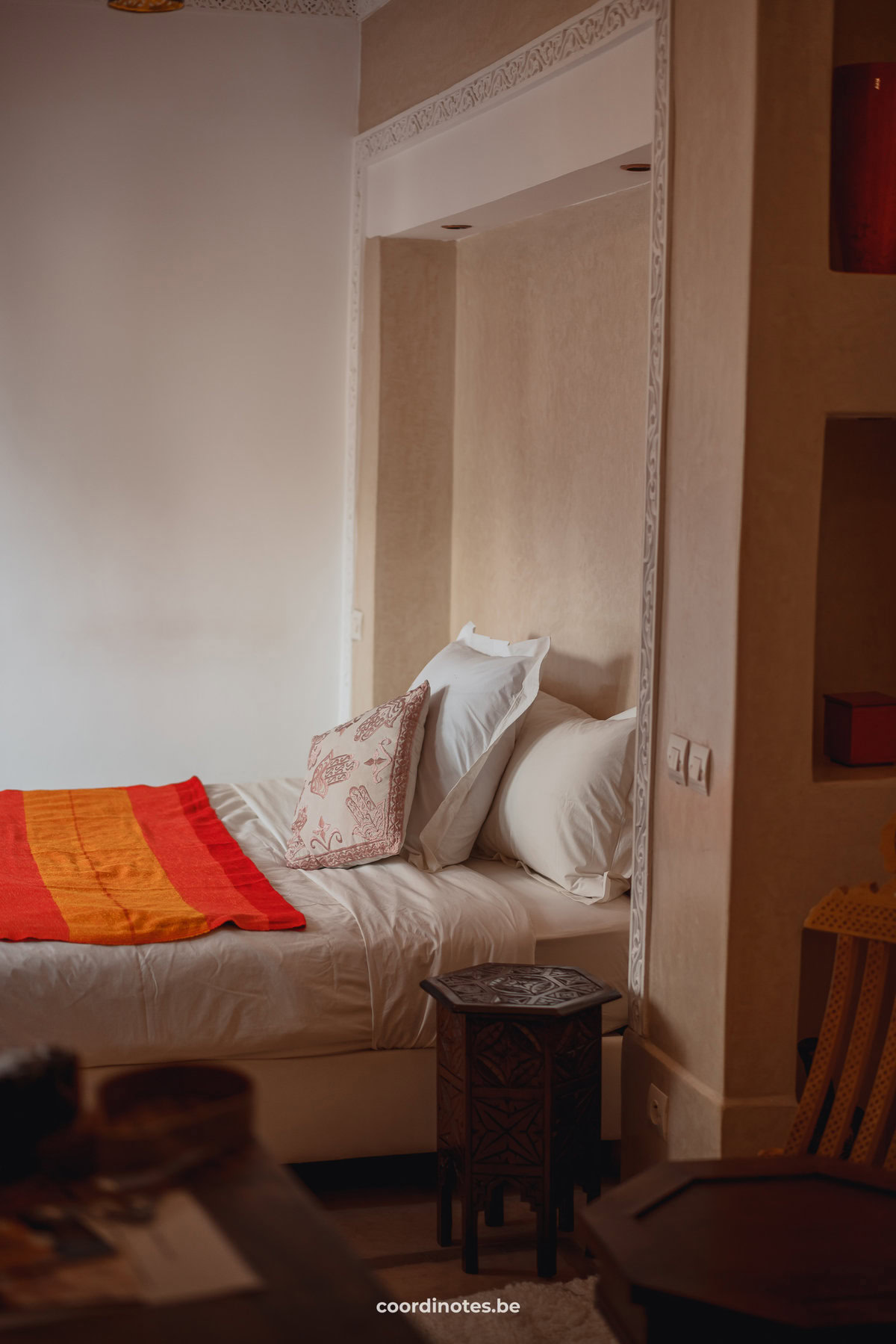 Een bed voor een beige muur met een oranje rood laken in Riad Dar Ten