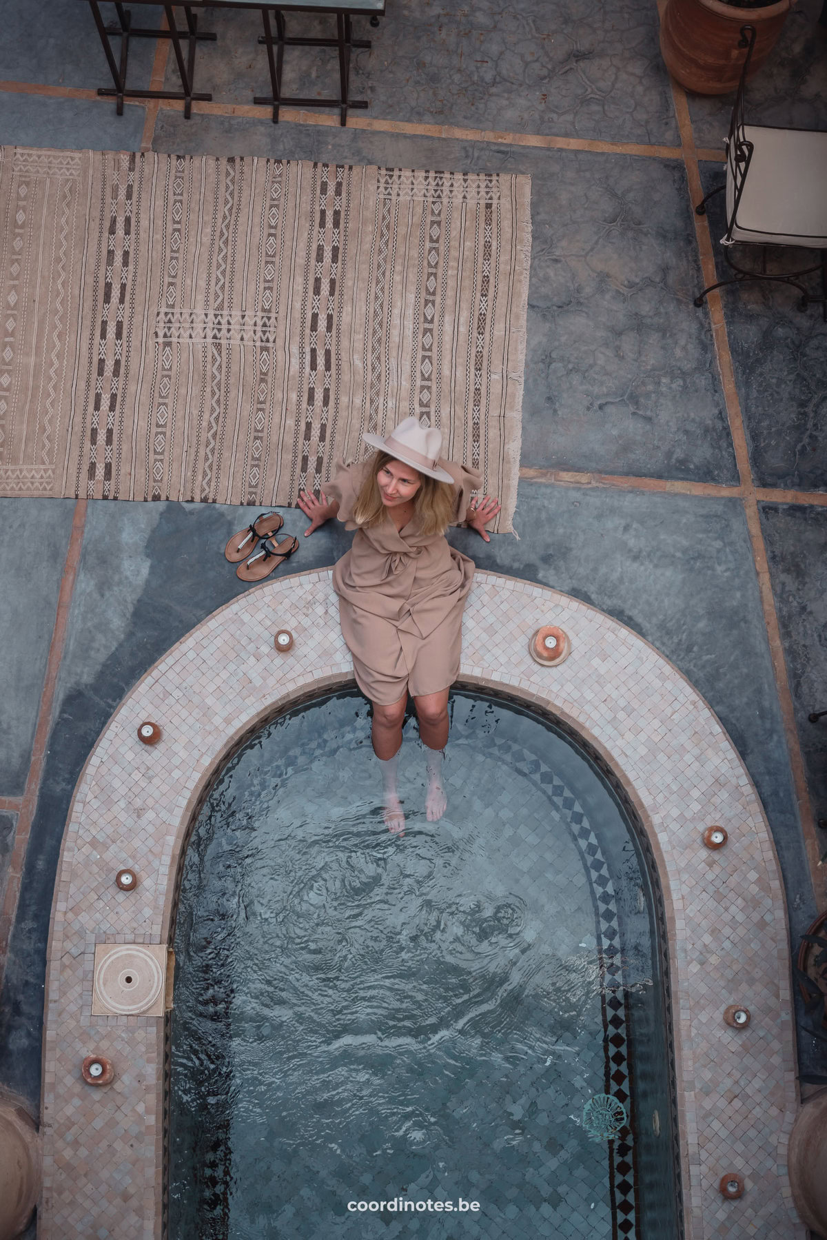 Sarah sitting on the edge of the oval pool of Riad Dar Ten with candles on the side and a carpet on the floor next to her.