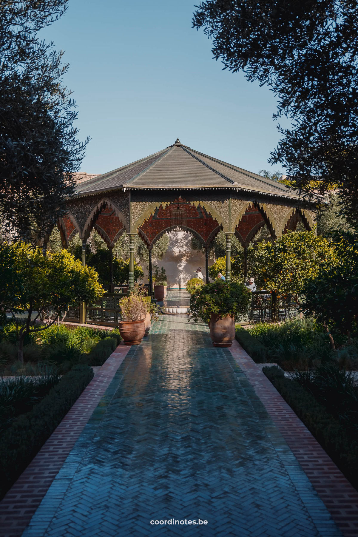 Een pad naar het paviljoen in Le jardin Secret omgeven door bomen en planten