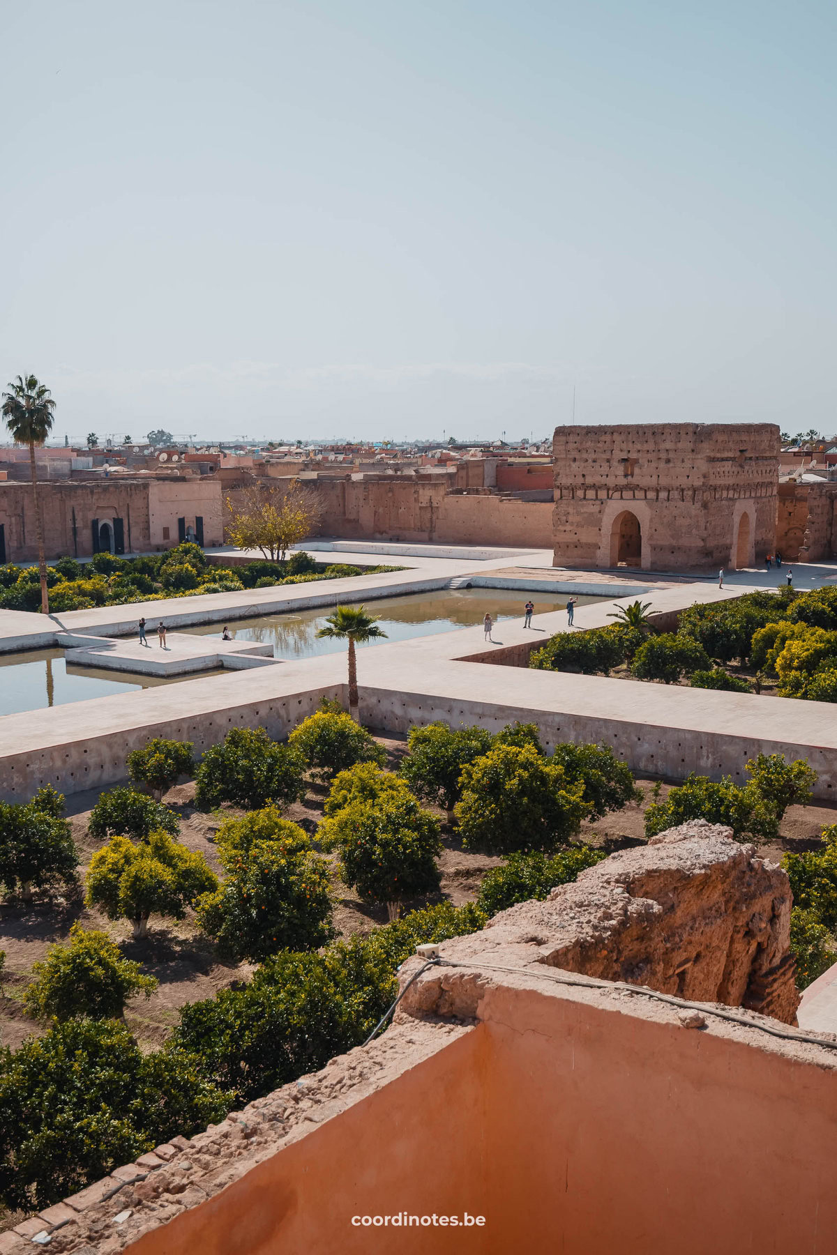 The big square of El Badi Palace with a big pool in the middle and multiple parts with bushes and plants.