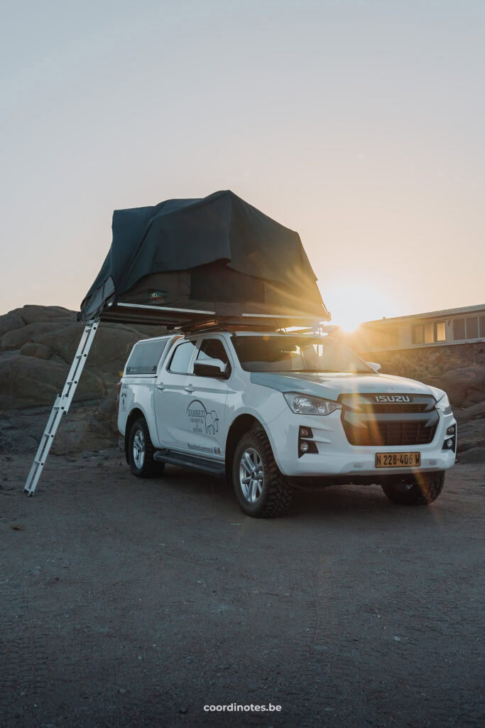 Our white pick-up truck with open rooftop tent at Shark Island Camping with the sun setting behind.