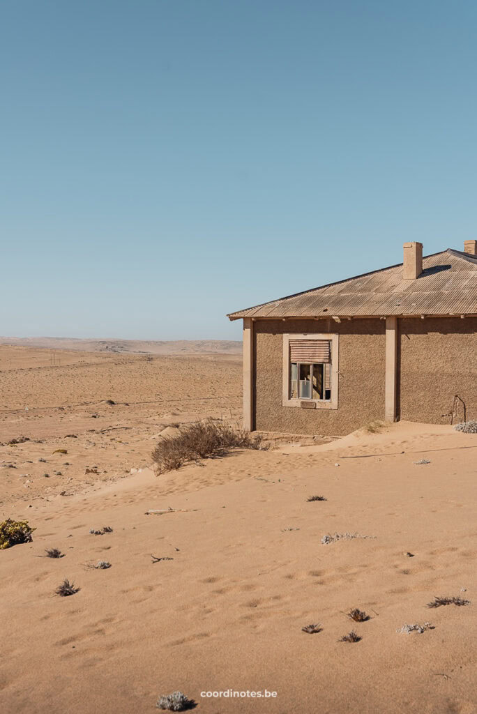 An abandoned house surrounded by sand.