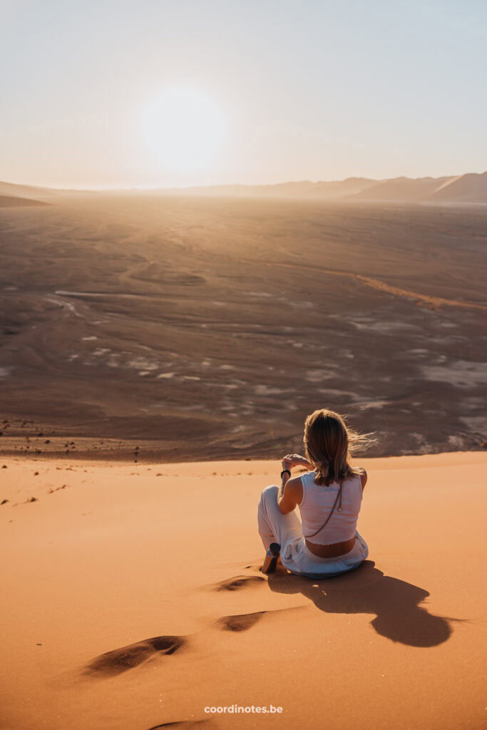 Sarah sitting on the Dun 45 sand dune while watching over sunset and the desert in the background