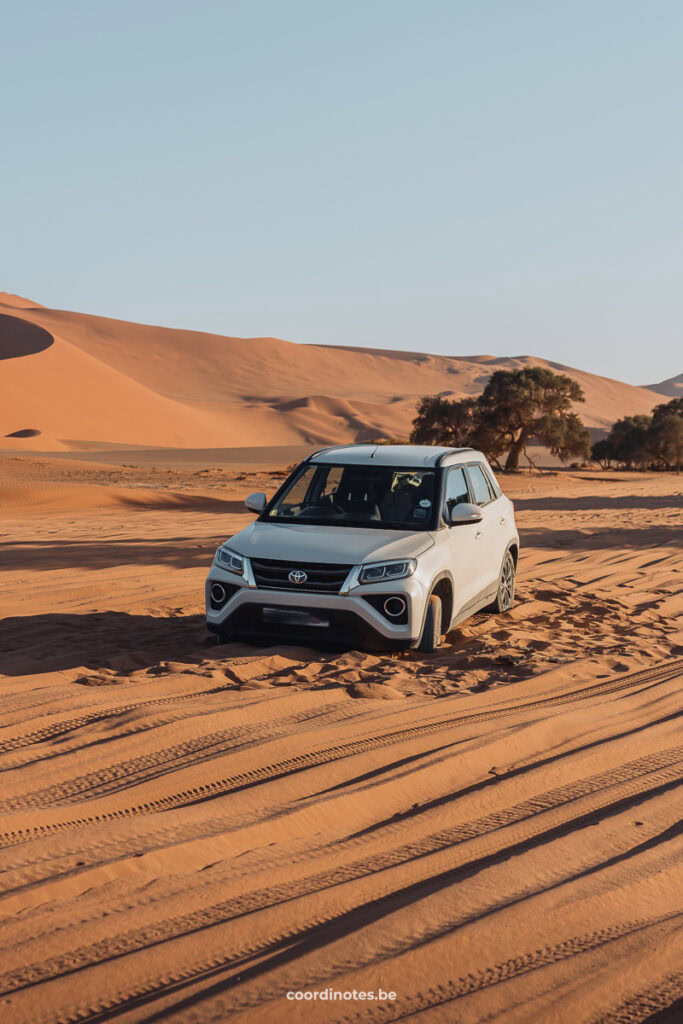 A white car stuck in the sand with some sand dunes in the background.