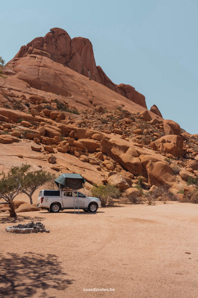 Our white pick-up truck with open rooftop tent in front of a huge red granite mountain at Spitzkoppe Camp Site