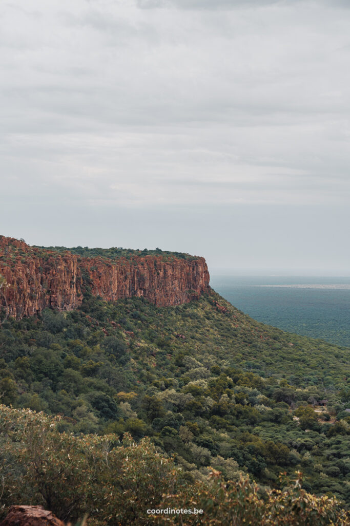 A huge orange cliff amidst a large plane filled with green trees and bushes.