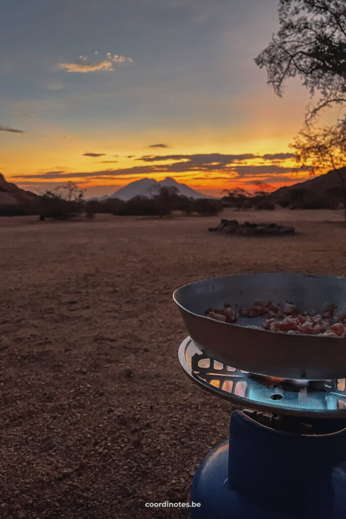 A pan with bacon on a gaspit on a gas bottle with a beautiful sunset in the background.