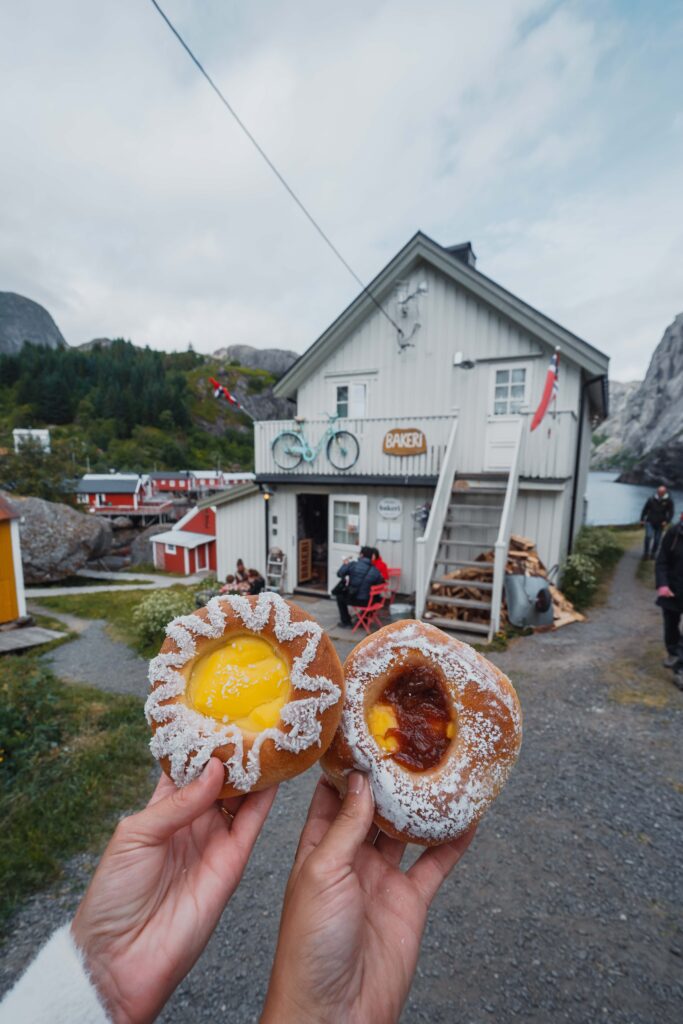 2 handen die 2 gebakjes vasthouden voor een wit bakkerijtje in de achtergrond in Nusfjord