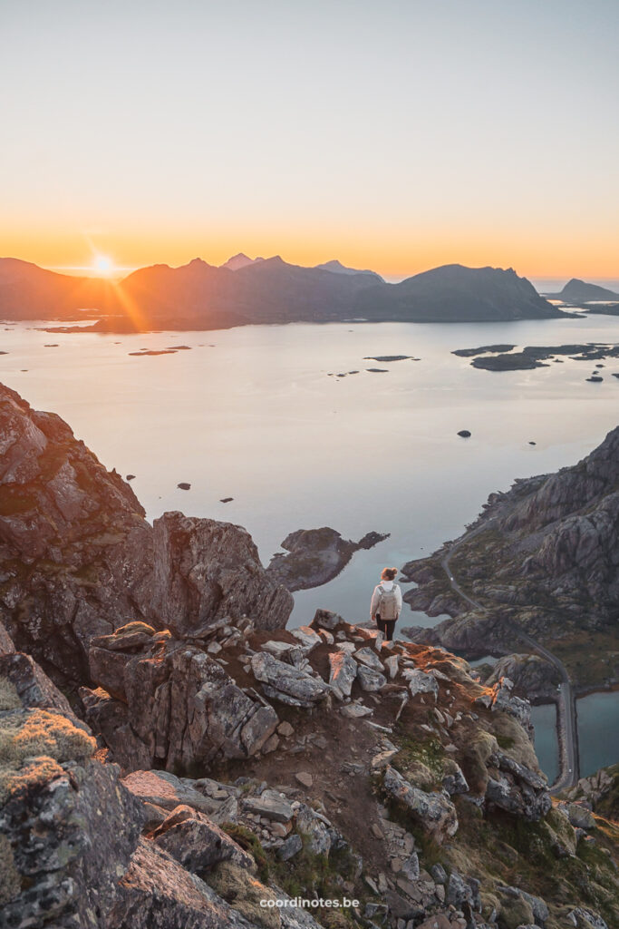 Sarah on top of Festvågtind watching over the fjord, the mountains and the sunset in the background