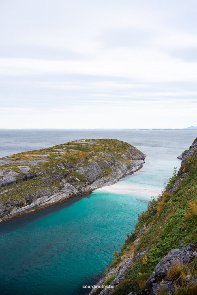 Coastal landscape with turquoise water in a narrow inlet between rocky cliffs and a pale sky above