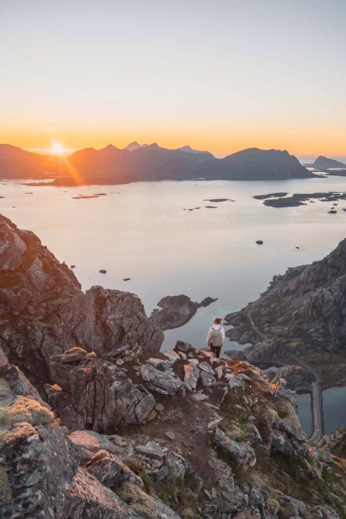 Sarah op de top van Festvagtind, met het fjord, bergen en de zonsondergang op de achtergrond.