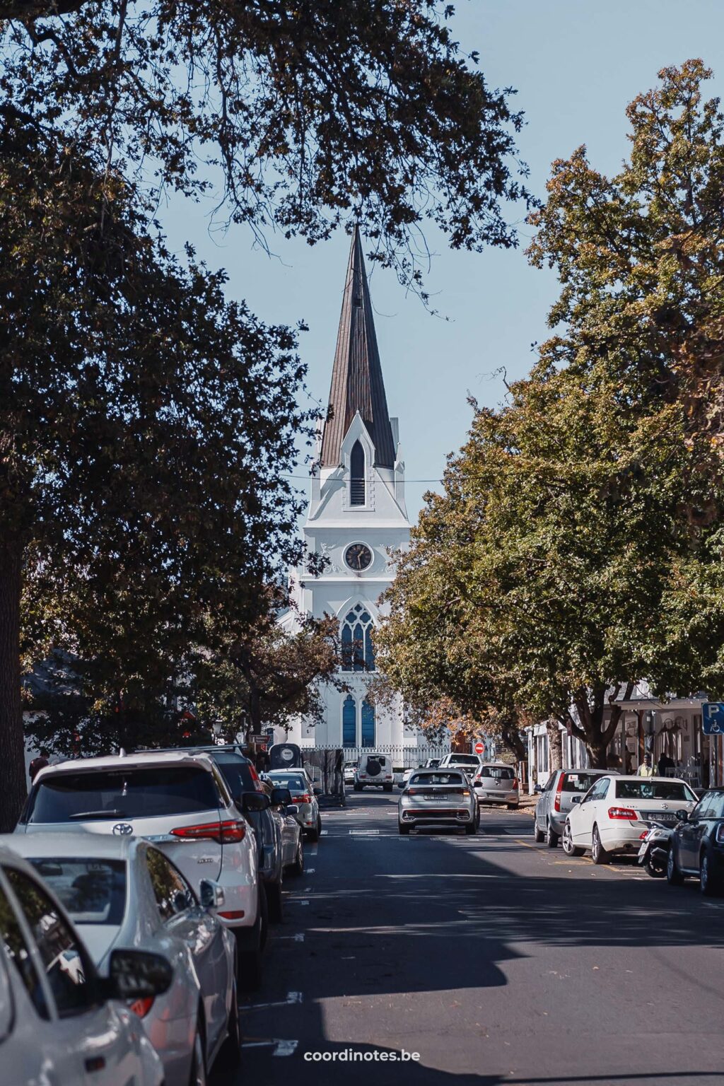 Een straat met bomen en auto's langs de weg met in de achtergrond de witte kerk van Stellenbosch