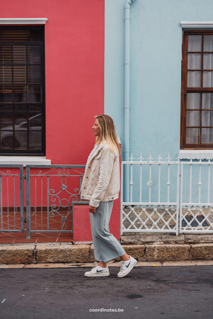 Sarah voor een muur die links roos en rechts blauw geschilderd is in Bo-Kaap