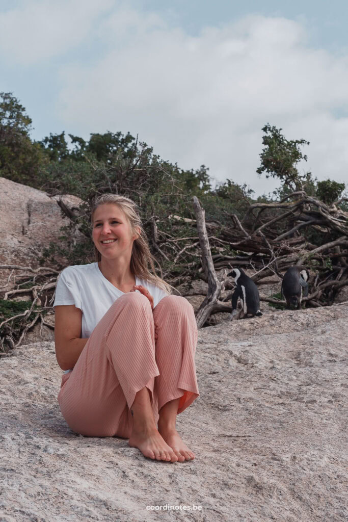 Sarah die op een rots zit naast twee Afrikaanse pinguïns op Boulders Beach