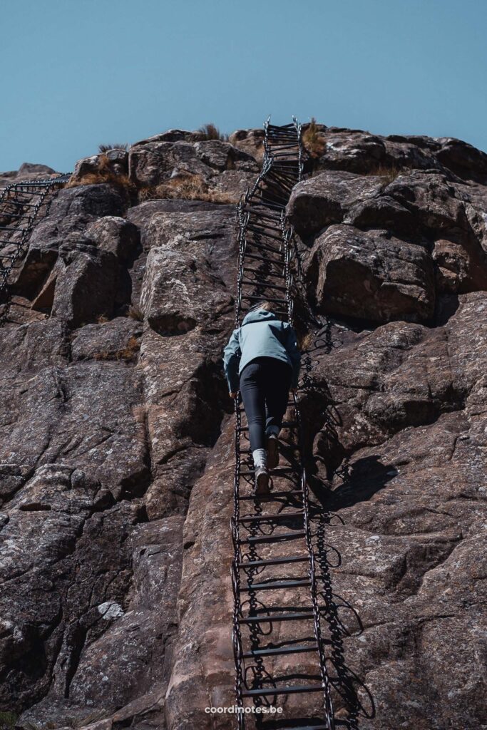 Sarah die een hoge kettingladder opklimt op een hoge rots in Drakensberg naar de Tugela Falls