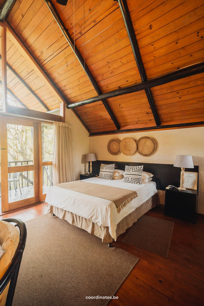 Een kamer bij Mantenga Lodge met een bed, een houten plafond, decoratie boven het bed en een deur naar het balkon dat je door de raam kan zien.