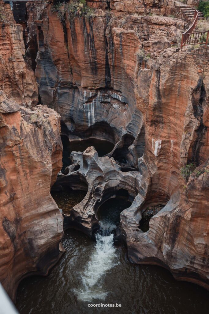 Een rivier die stroomt tussen hoge oranje rotsen waarin pothole's zijn ontstaan door erosie bij de Bourke's Luck Potholes