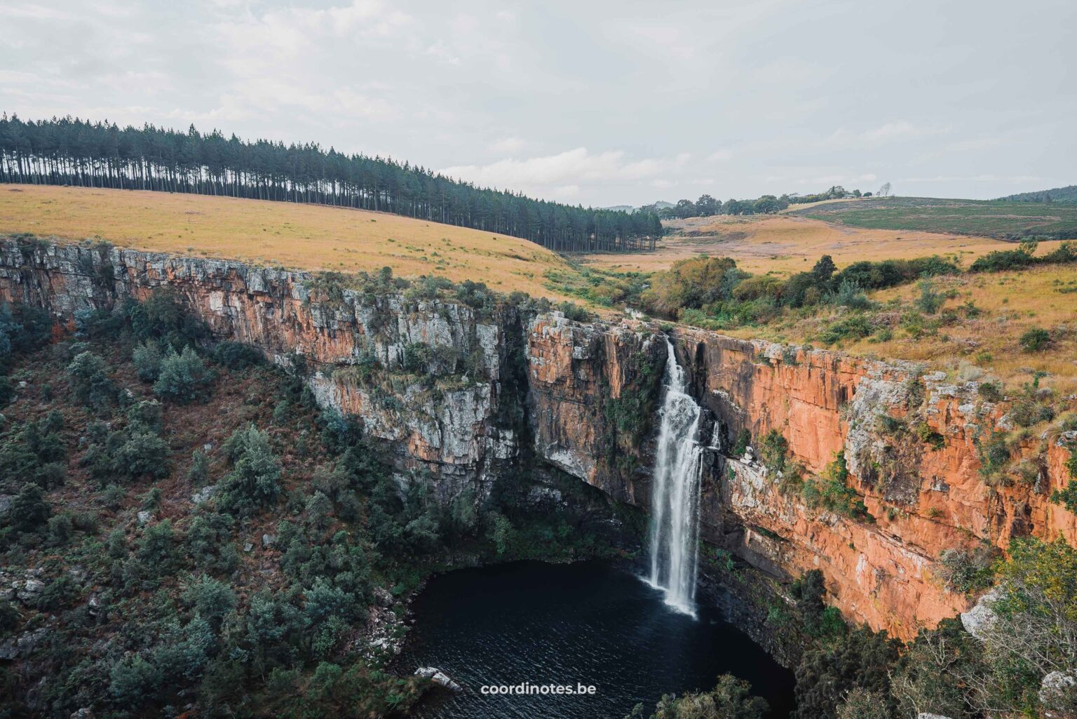 De Berlin falls waterval die naar beneden stort van een grote oranje klif in een groen glooiend landschap