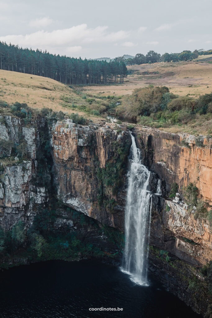 The Berlin Falls waterfall, tumbling down a huge orange wall with a grassy landscape in the background