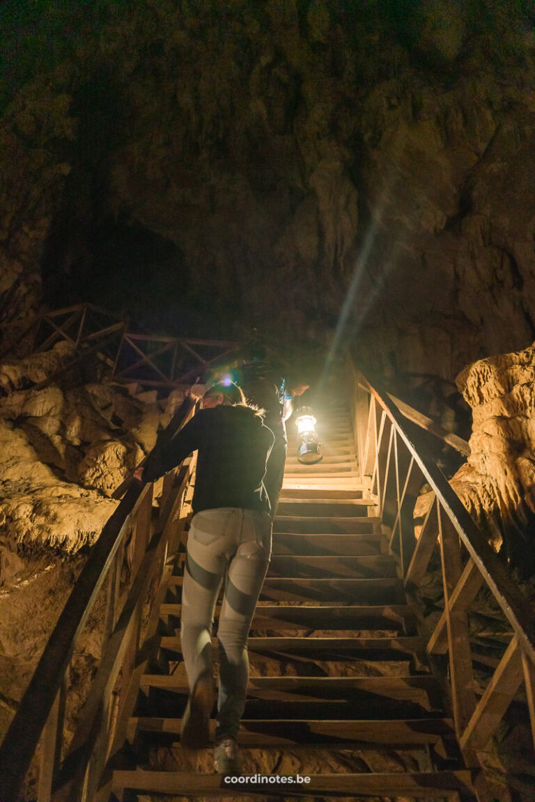 Sarah and our guide holding a gas lamp, walking up a wood stairs inside the Tham Lod Cave.