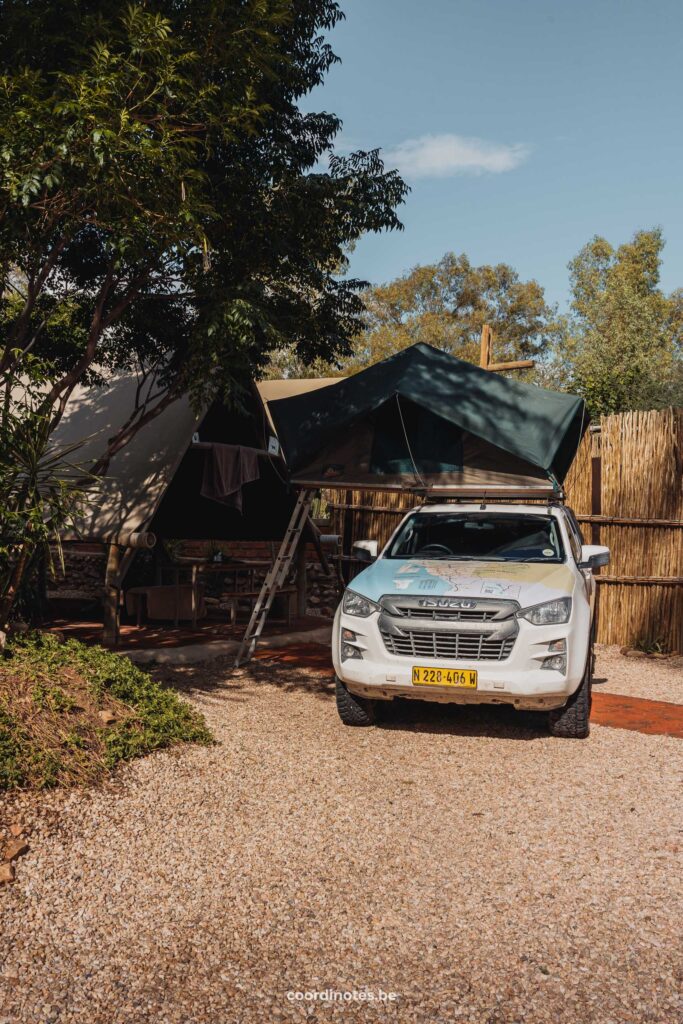 Our pick up truck with open roof tent next to the trees and wooden triangle hut at Urban Camp