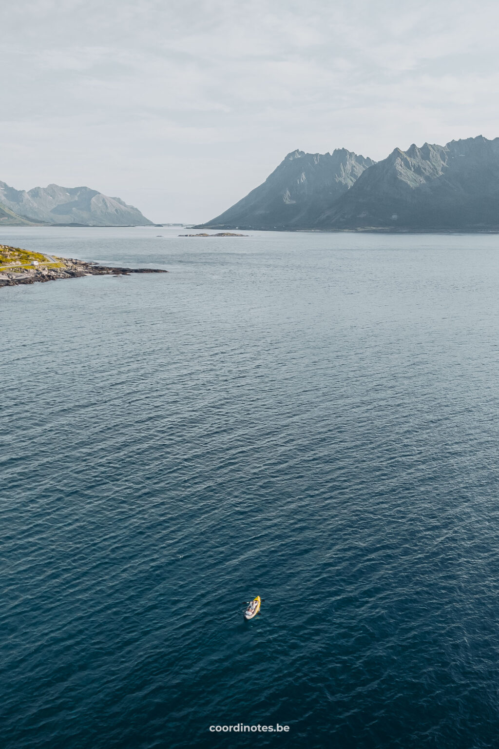 Een klein gele kayak op een fjord met de bergen op de achtergrond.